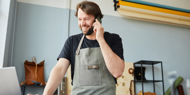 Small business owner wearing apron smiling on phone with Bizcap