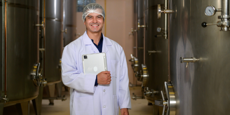 Small business owner in white lab coat holding tablet next to the beverage machinery