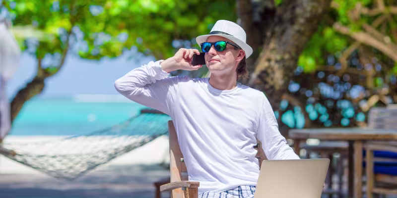 Island resort business owner sitting on beach on phone with broker