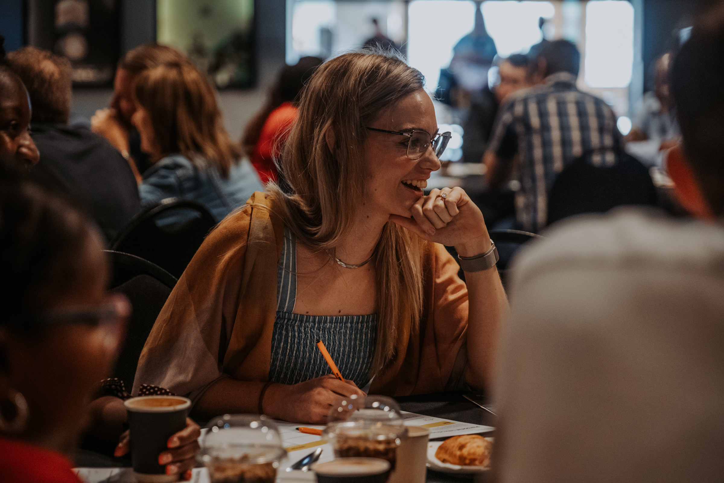 Woman at restory business breakfast event smiling while listening to someone speak at her table.