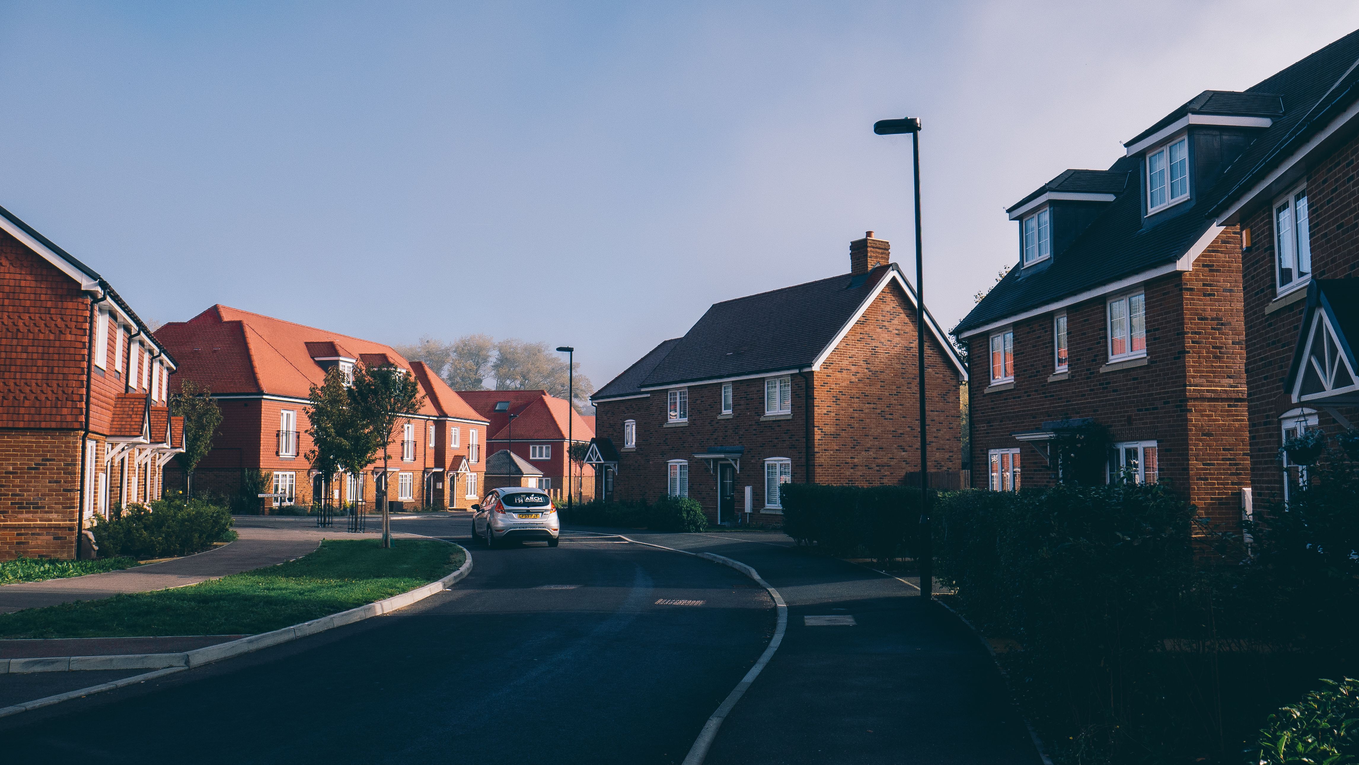 A modern British residential street of red brick houses with a parked car and street lighting