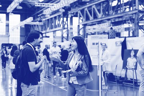 Two professionals engaging in a lively conversation during a networking event inside a large industrial-style venue.