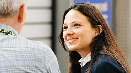 Smiling woman with long brown hair engaged in conversation with a man wearing a plaid shirt.
