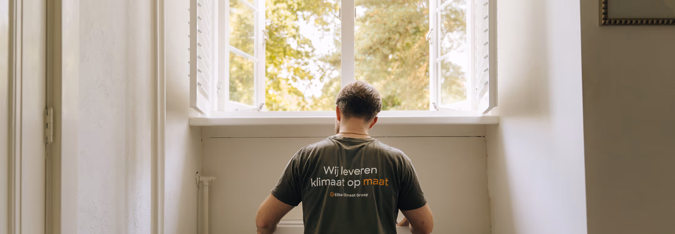 Monteur controleert een airco-unit in een lichte ruimte, als onderdeel van preventief onderhoud door Elite Klimaat Groep.