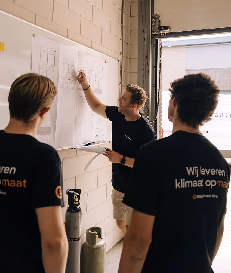 Installateurs bespreken een technisch installatieplan voor een warmtepomp in een werkplaats