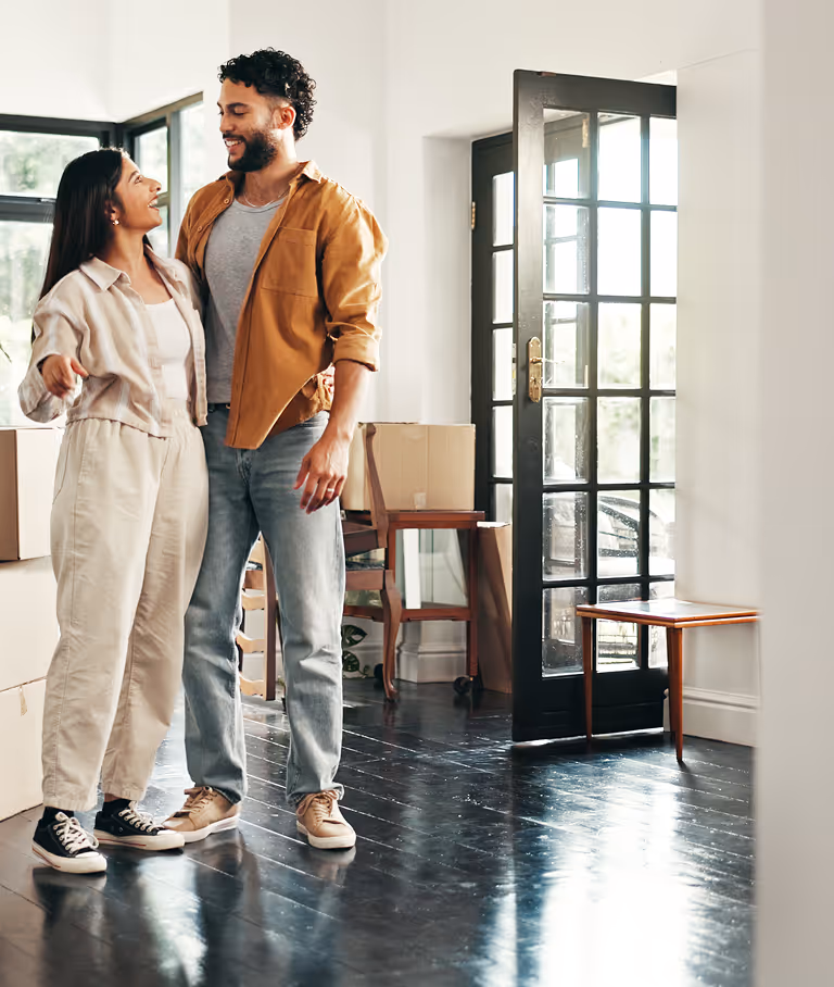 Koppel staat lachend in een lichte woning met verhuisdozen, symbool voor een duurzame woning