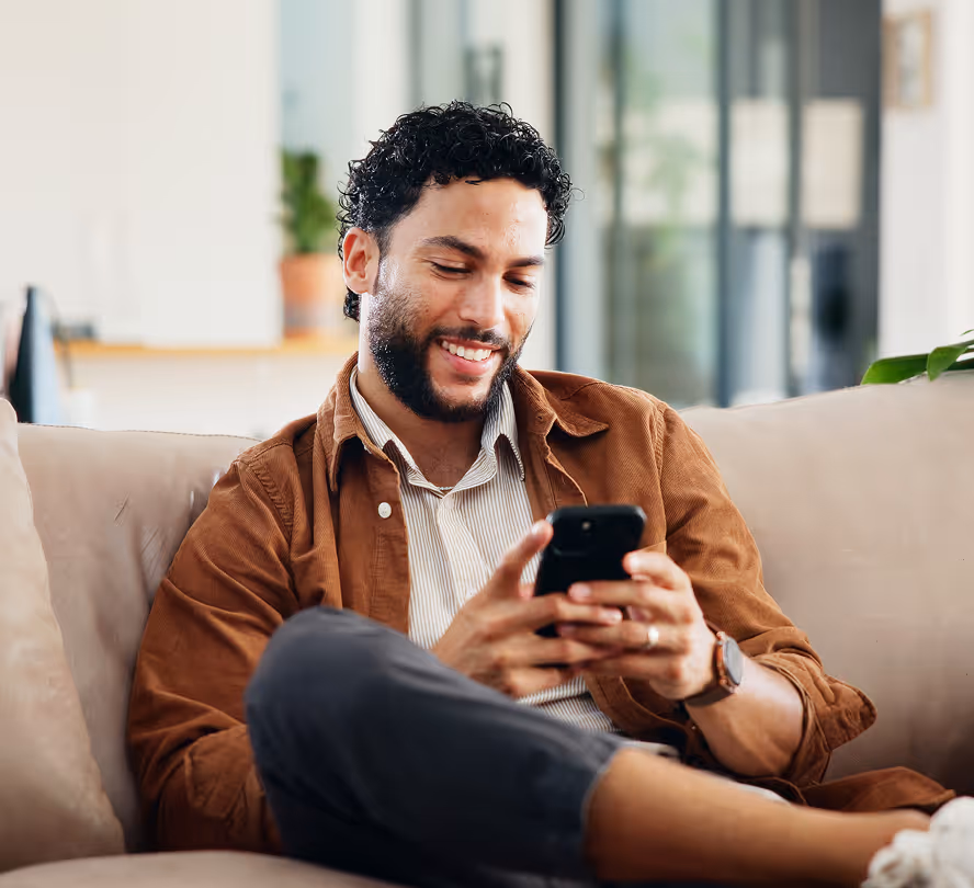 Man zit op de bank en bedient zijn warmtepomp met een smartphone.