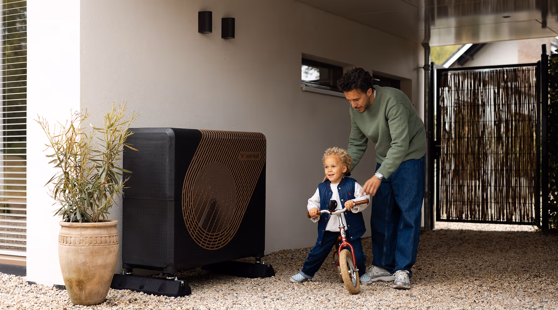Vader helpt een kind fietsen naast een buitenunit van een warmtepomp bij de woning.