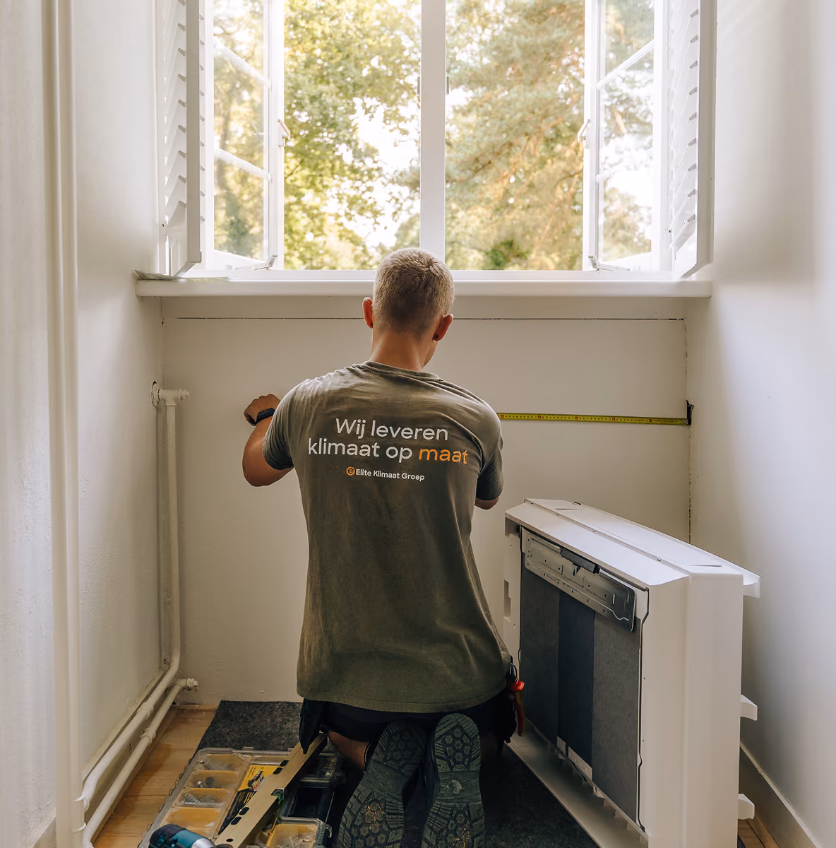 Monteur van Elite Klimaat Groep meet de wand onder een raam op voor de montage van een airco binnendeel