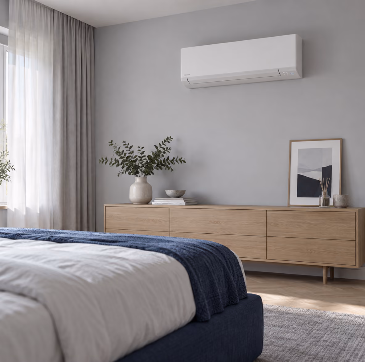 Toshiba Kazumi airco op een lichtgrijze wand boven een eiken ladekast in een rustige slaapkamer