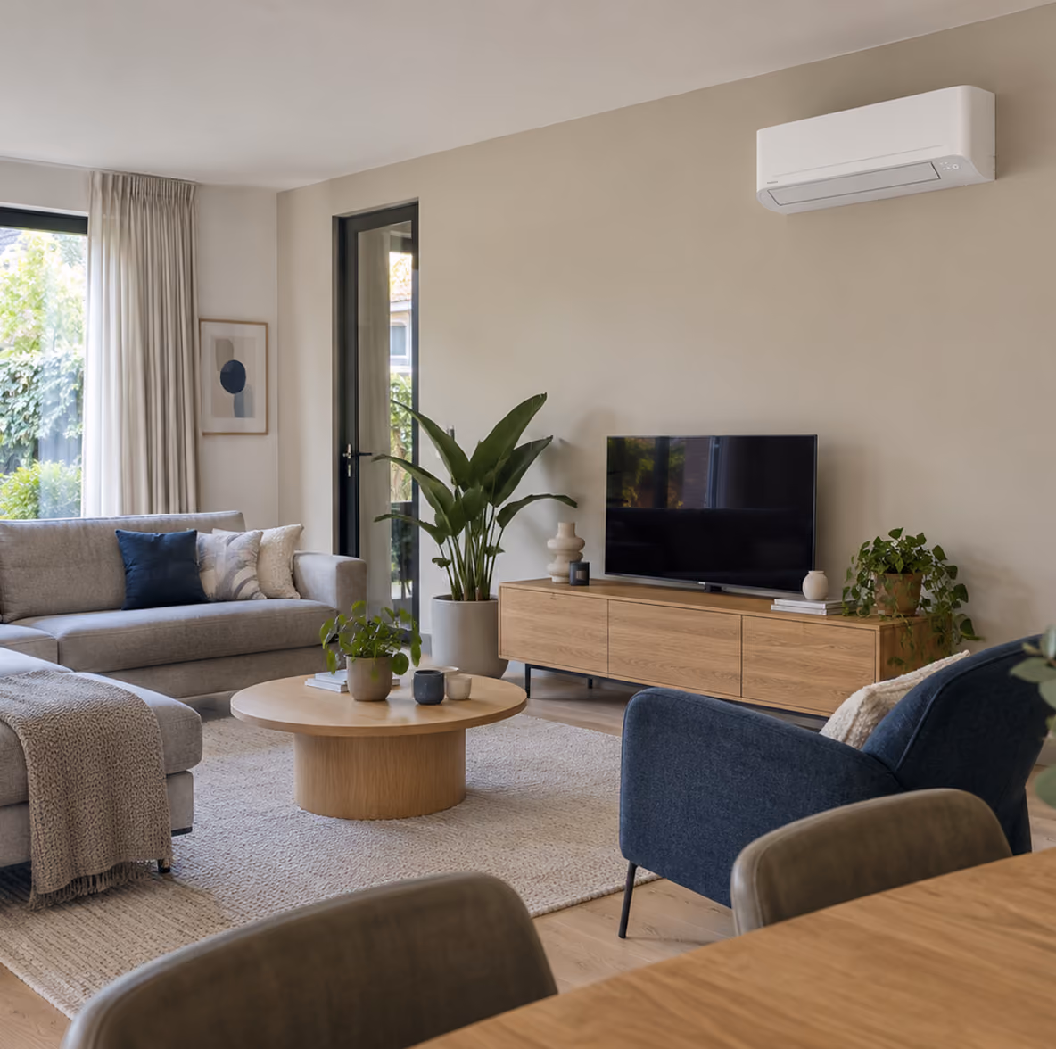 Toshiba Seiya airco boven een eiken tv-meubel in een lichte woonkamer met grijze bank en tuindeuren