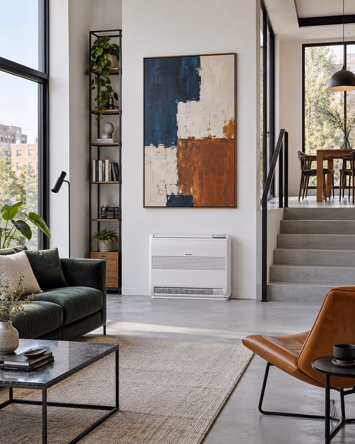 Toshiba vloermodel airco laag aan de wand onder een abstract schilderij in een loft met groene bank en betonnen trap