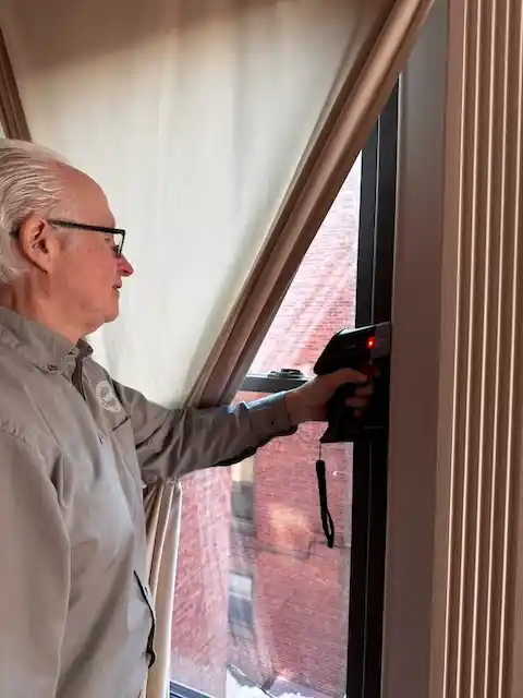 Jack Mason using a handheld device to scan or test a window inside a building.