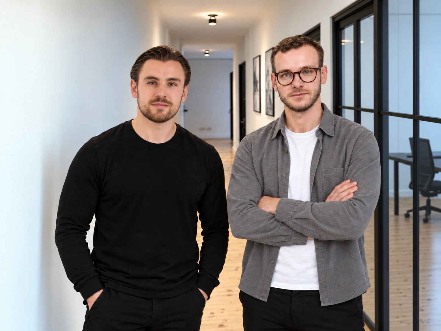 Zwei junge Männer mit verschränkten Armen, einer mit kurzem braunem Haar und Smartwatch, der andere mit dunklem Haar zurückgekämmt, vor weißem Hintergrund.