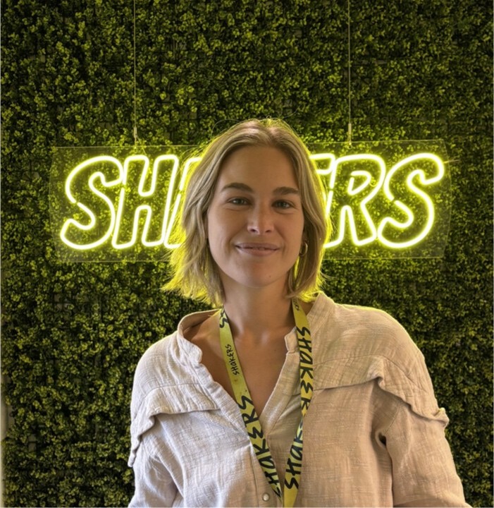 Mujer joven con cabello largo y oscuro, sonriendo, vistiendo un suéter negro, sobre fondo claro.
