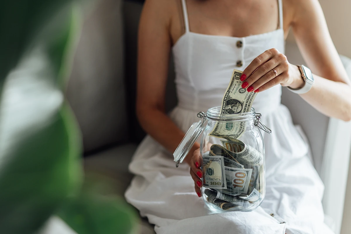 Young woman reviews bridal makeup cost and hand cash from a jar.
