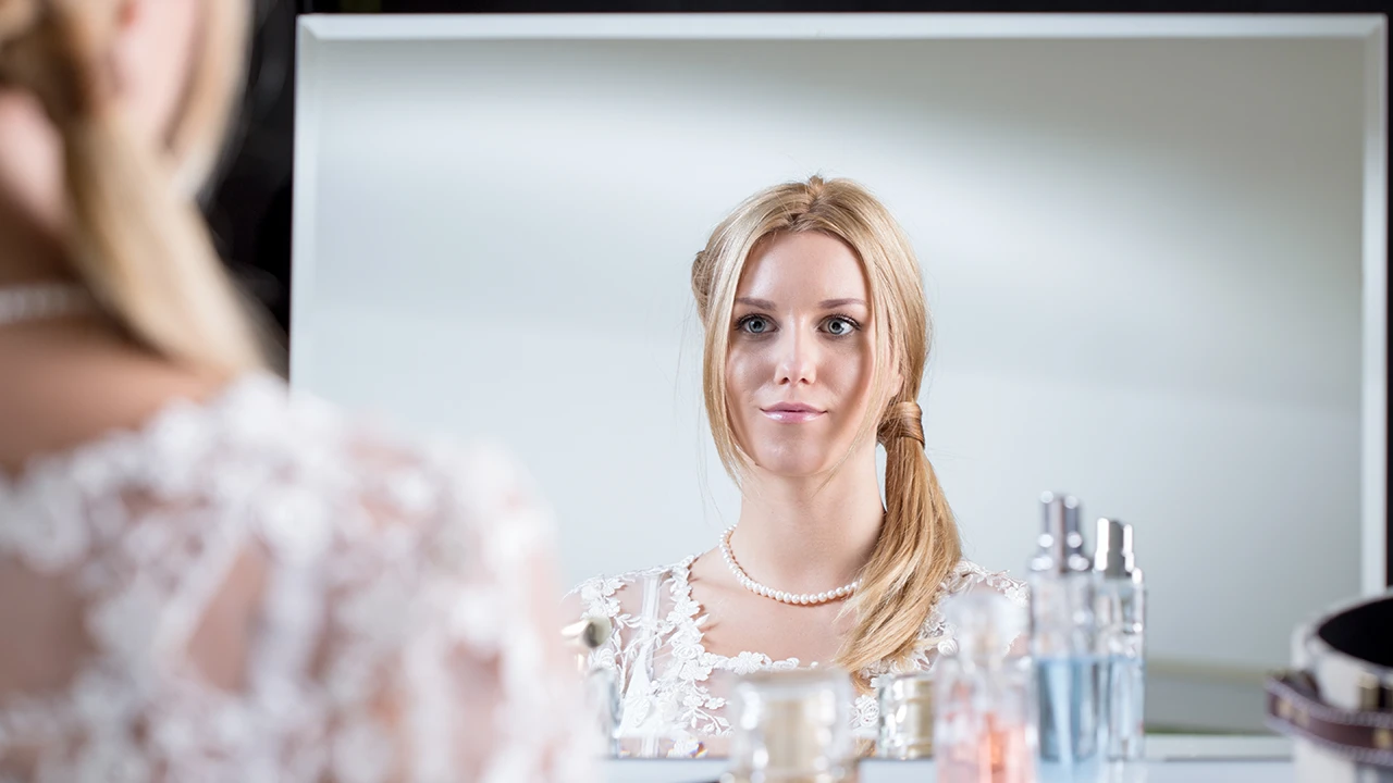 Makeup artist applying bridal makeup at home with the bride looking at the mirror.