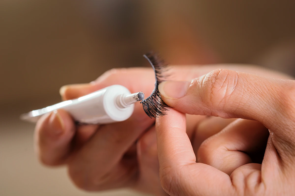 Beginner applying thin layer of lash glue to false lash band.