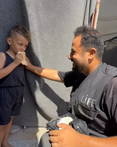 Geste solidaire Ă Gaza : un bĂ©nĂ©vole LIFE offre du pain Ă un enfant lors dâune distribution humanitaire. Aider gaza, soutien palestine.