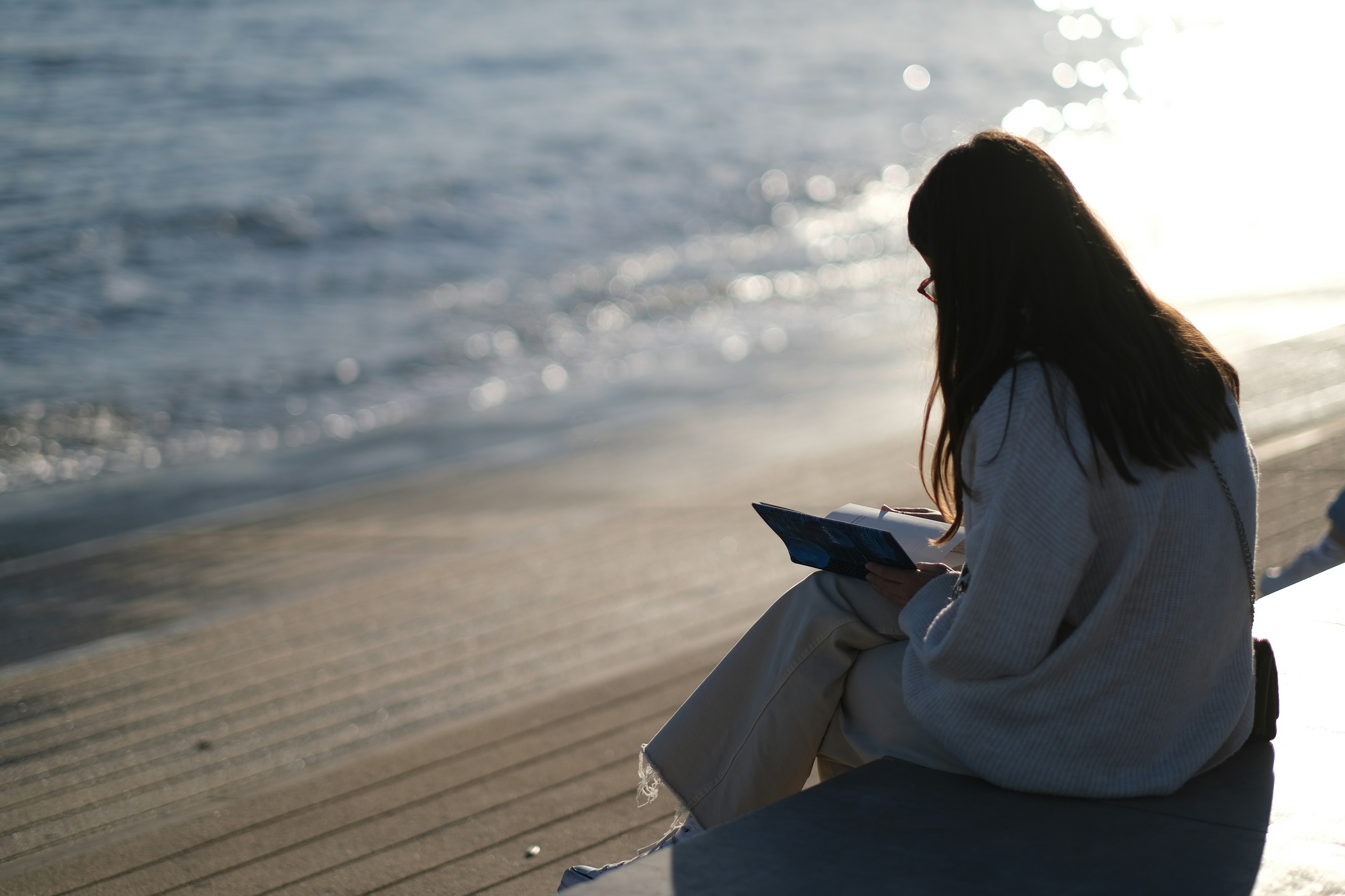 Woman sitting by the beach reading a book