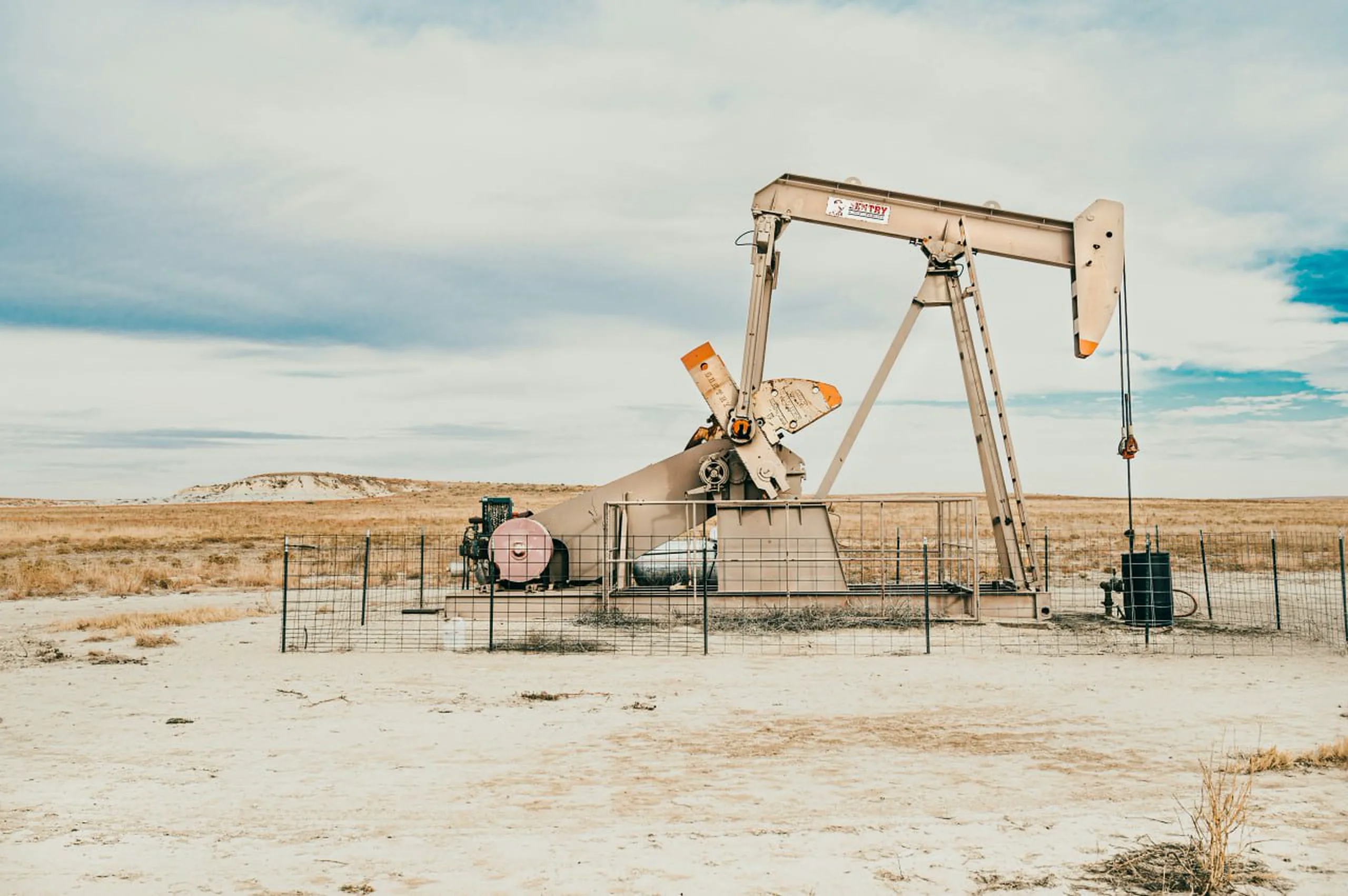 Entry pumpjack in a New Mexico field beneath a broad cloudy sky