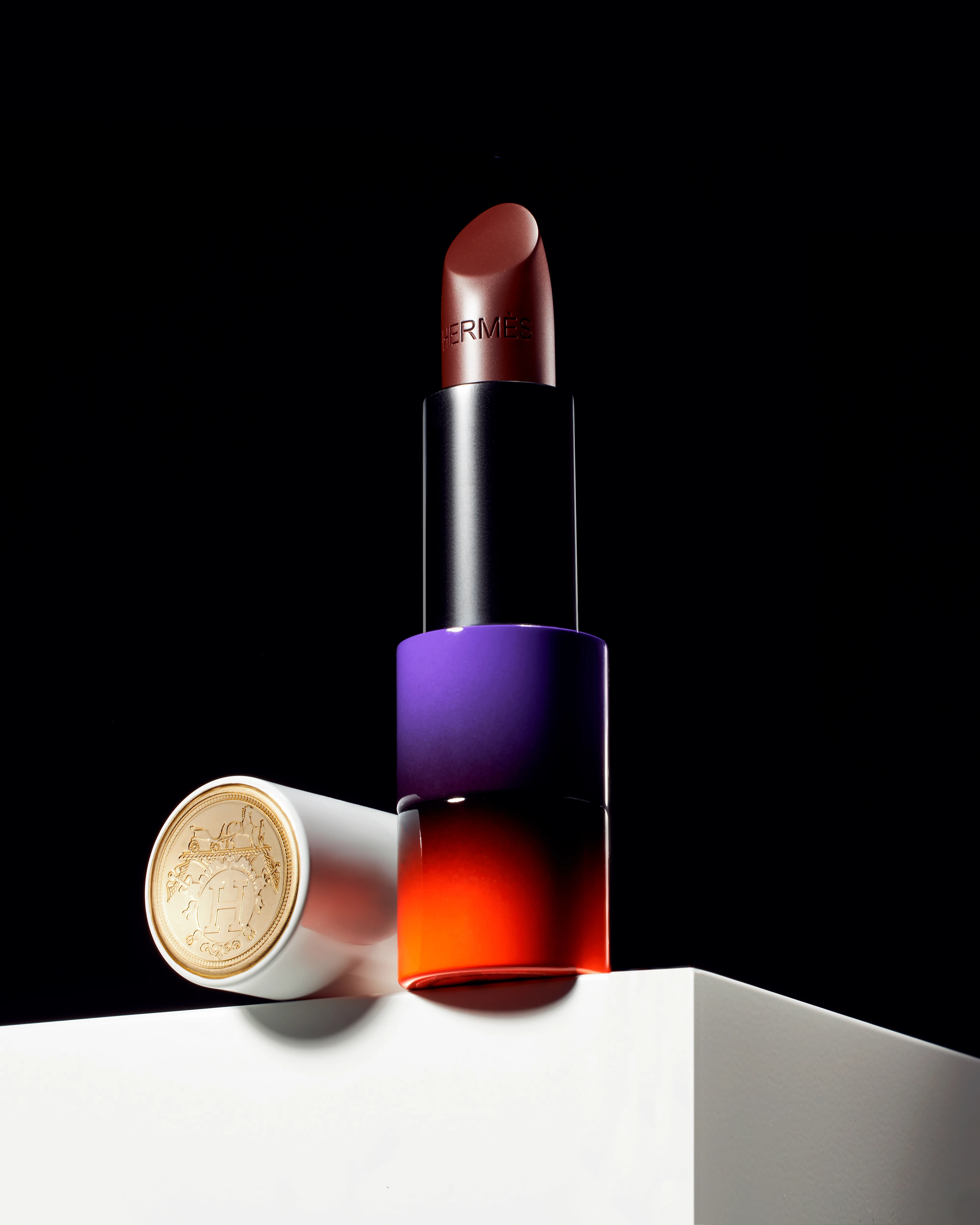 A bottle of red lipstick with a white cup next to it.