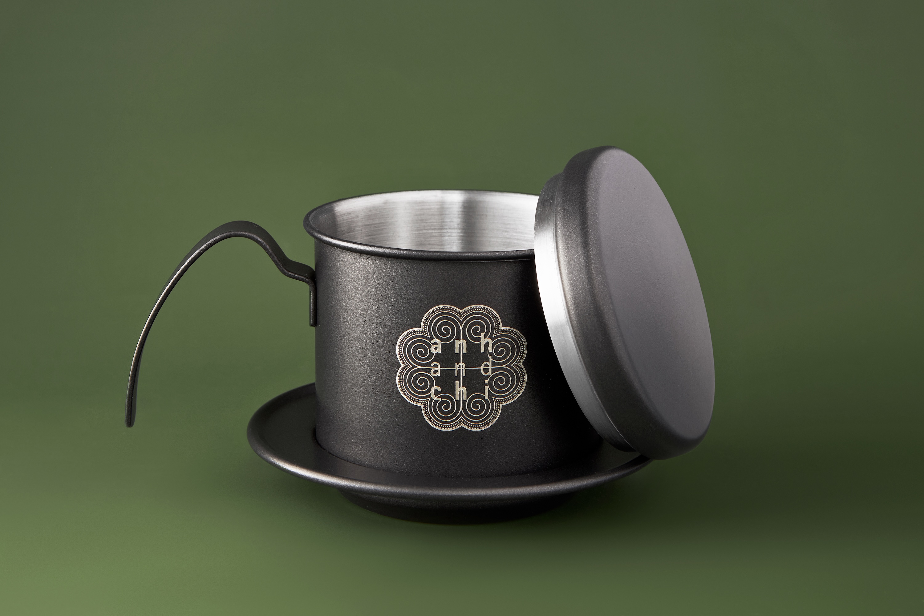 A black teapot with a silver lid on a green background.