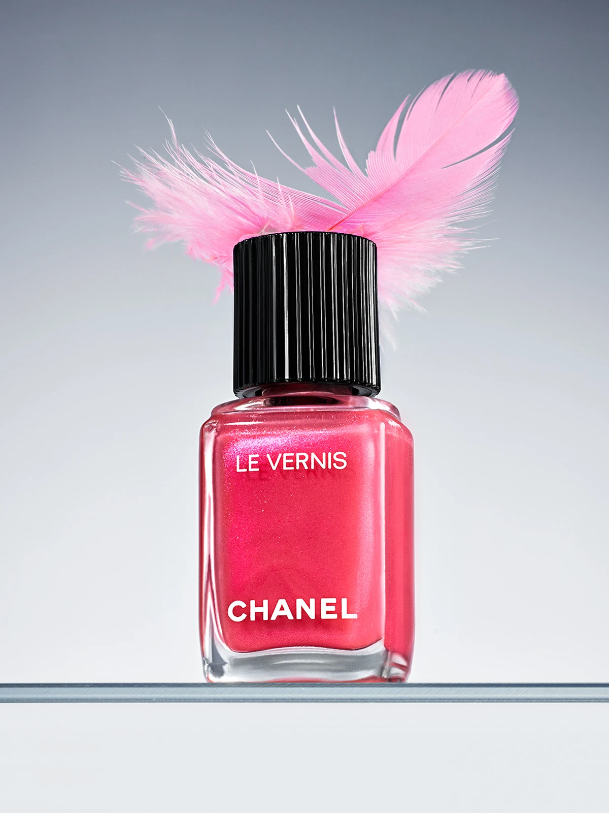A bottle of Chanel nail polish with a pink feather on top.