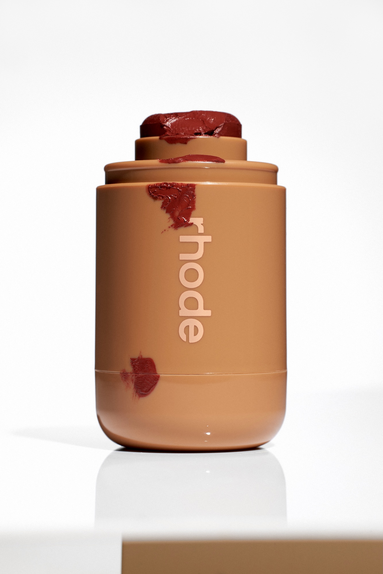 A brown bottle of Rhode lipstick with a red stain on it.