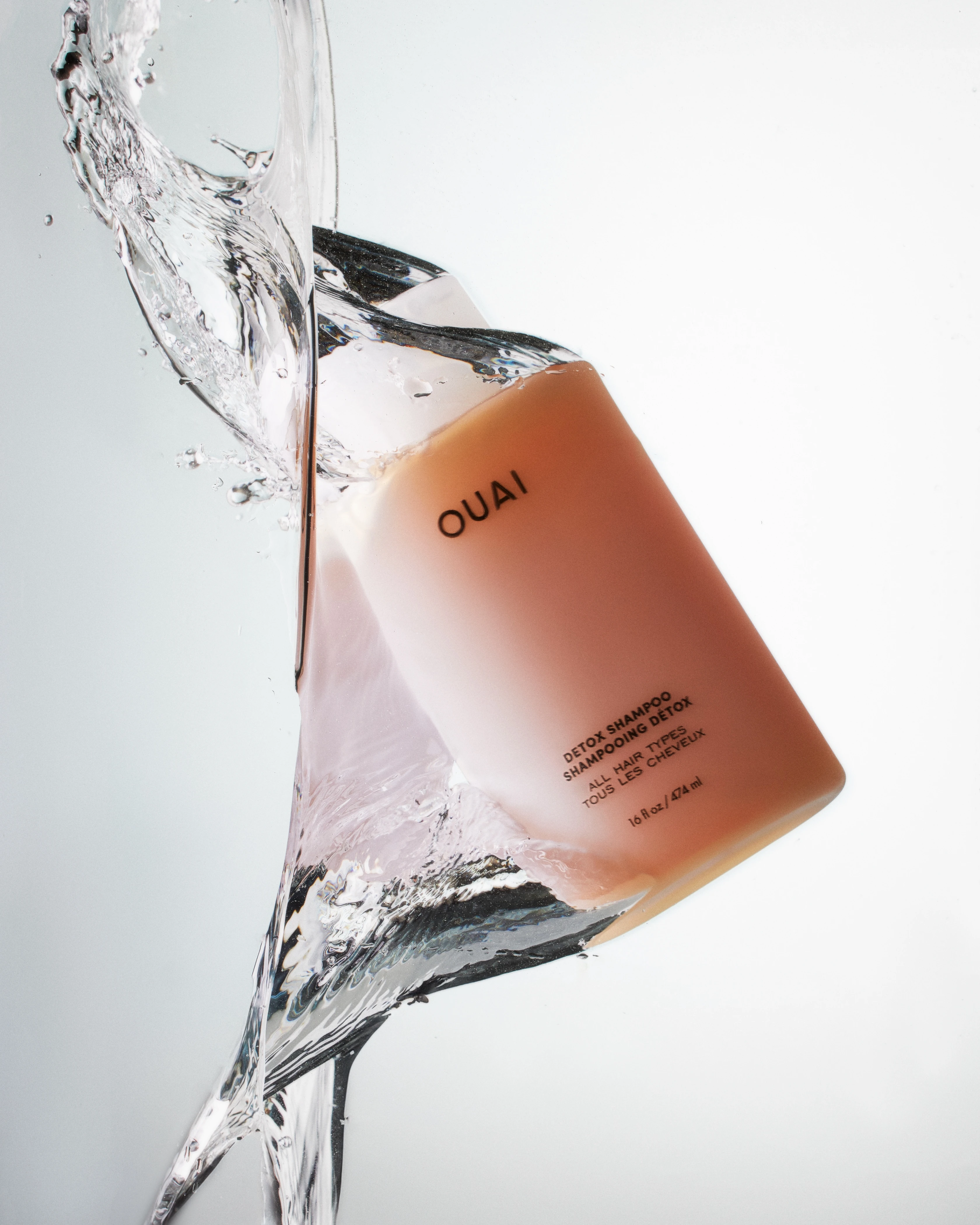 A bottle of Ouai perfume is shown in a waterfall of water.