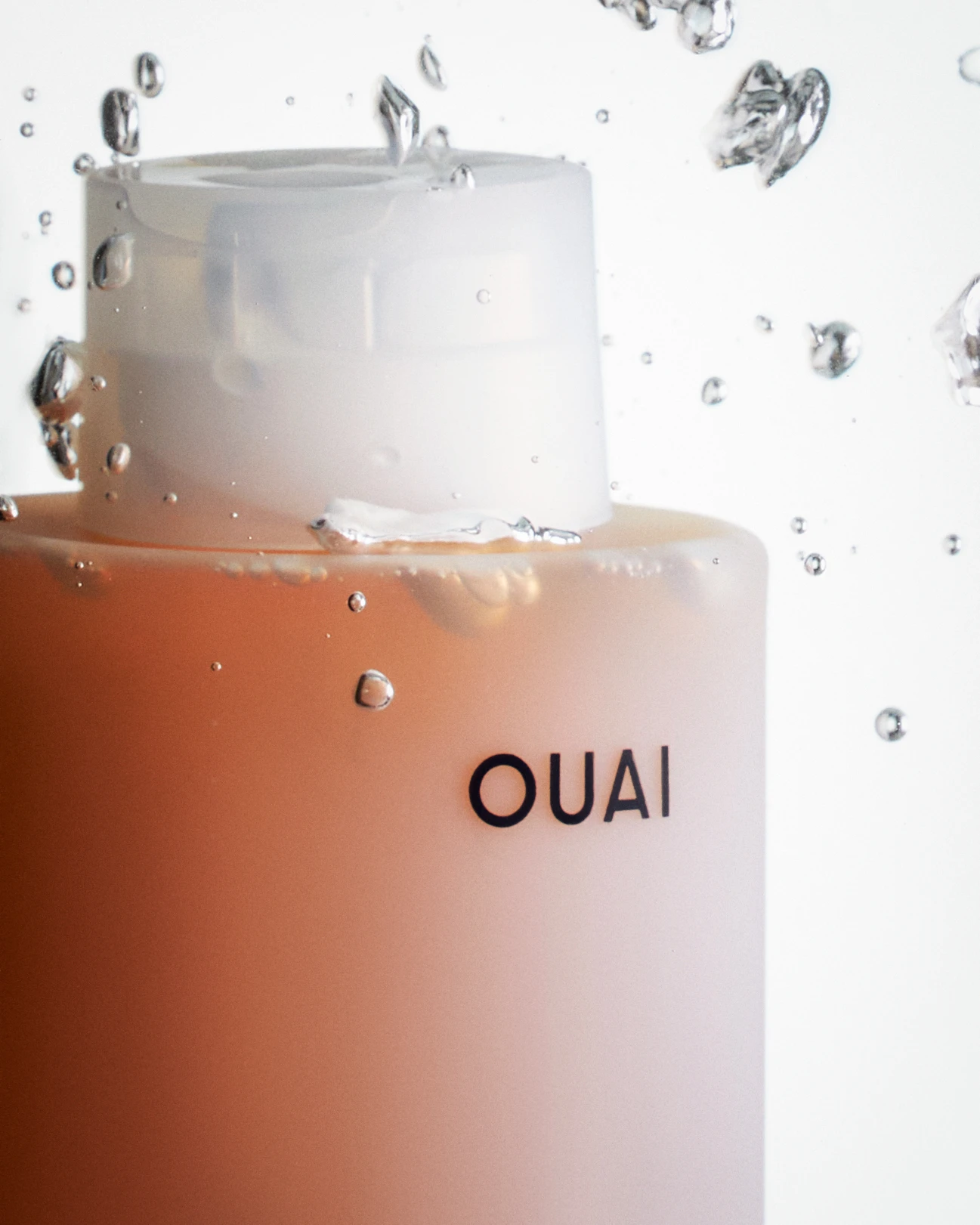 A bottle of Ouai lotion with water droplets in the background.