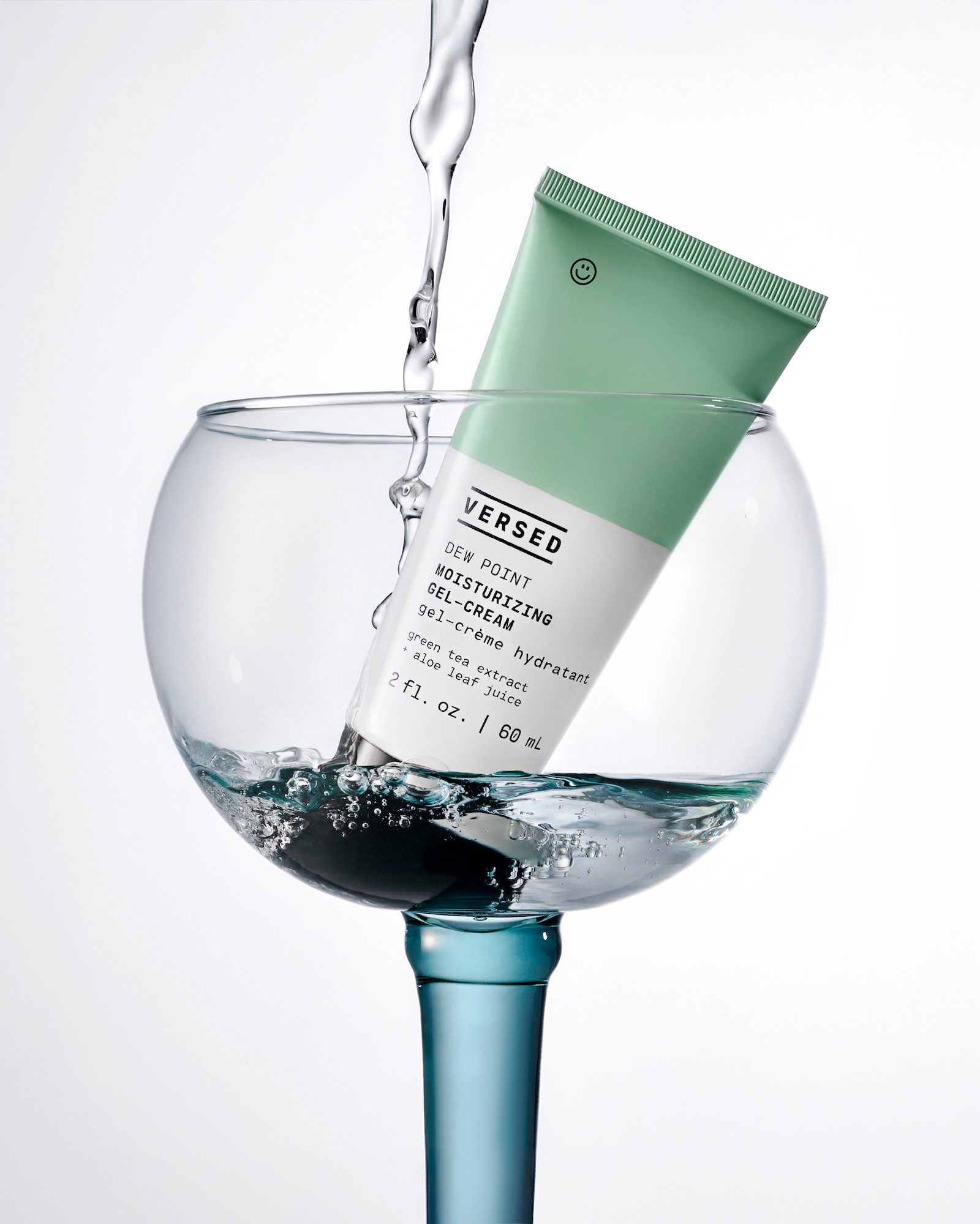 A green bottle of Versed moisturizing serum is in a glass of water.