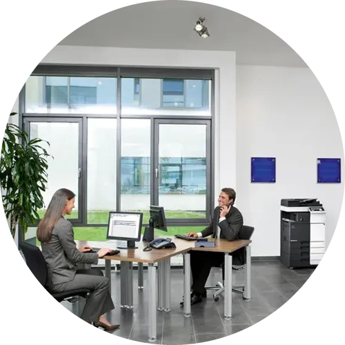 two people working at desks in an office with a copier