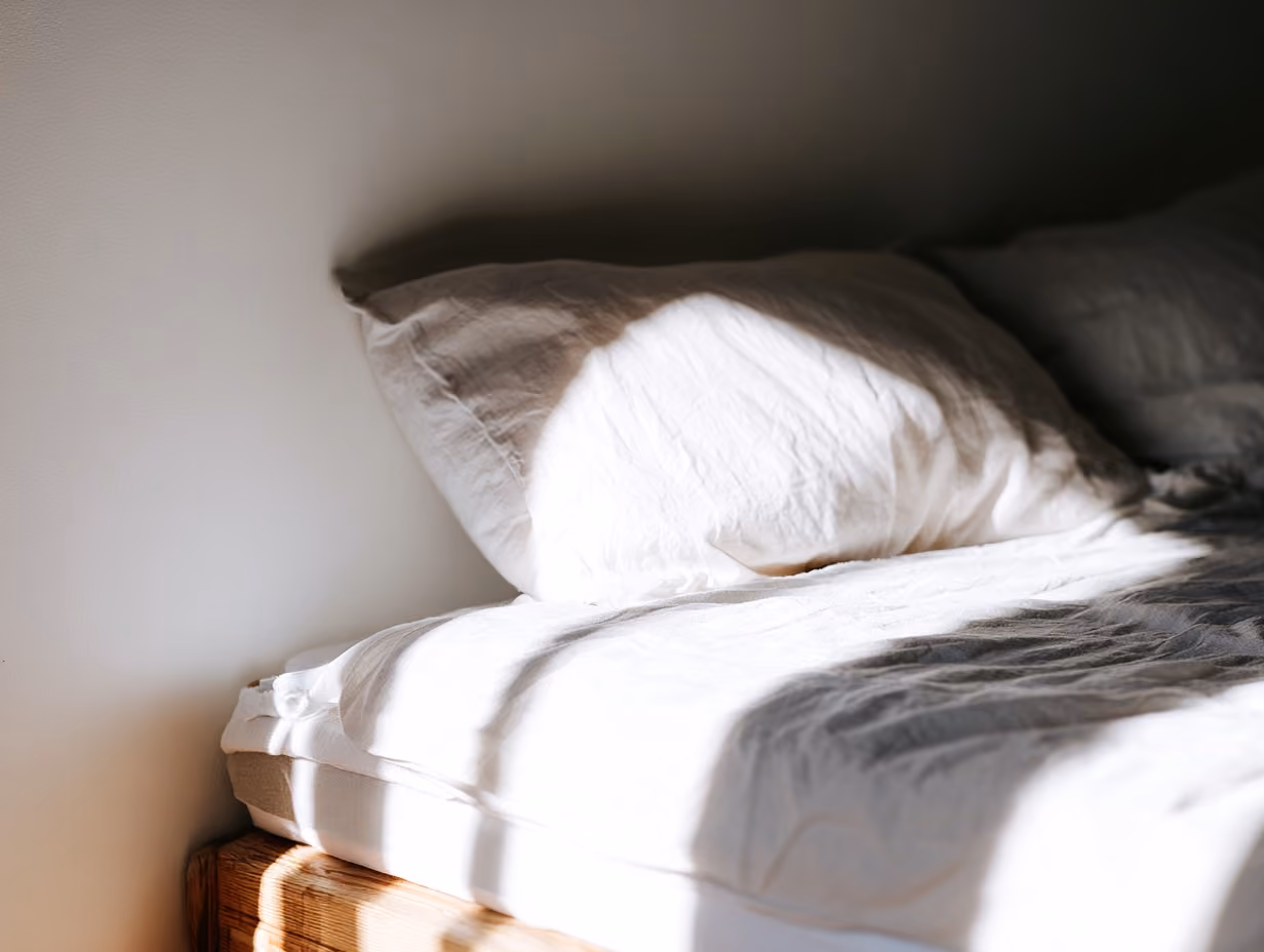 A neatly made guest bedroom in a short-term rental with a medium-firm mattress, crisp white bedding, two pillows, and a visible mattress protector edge, shot in soft natural daylight. Alt text: "Medium-firm queen mattress made up with white bedding in an Airbnb guest bedroom.