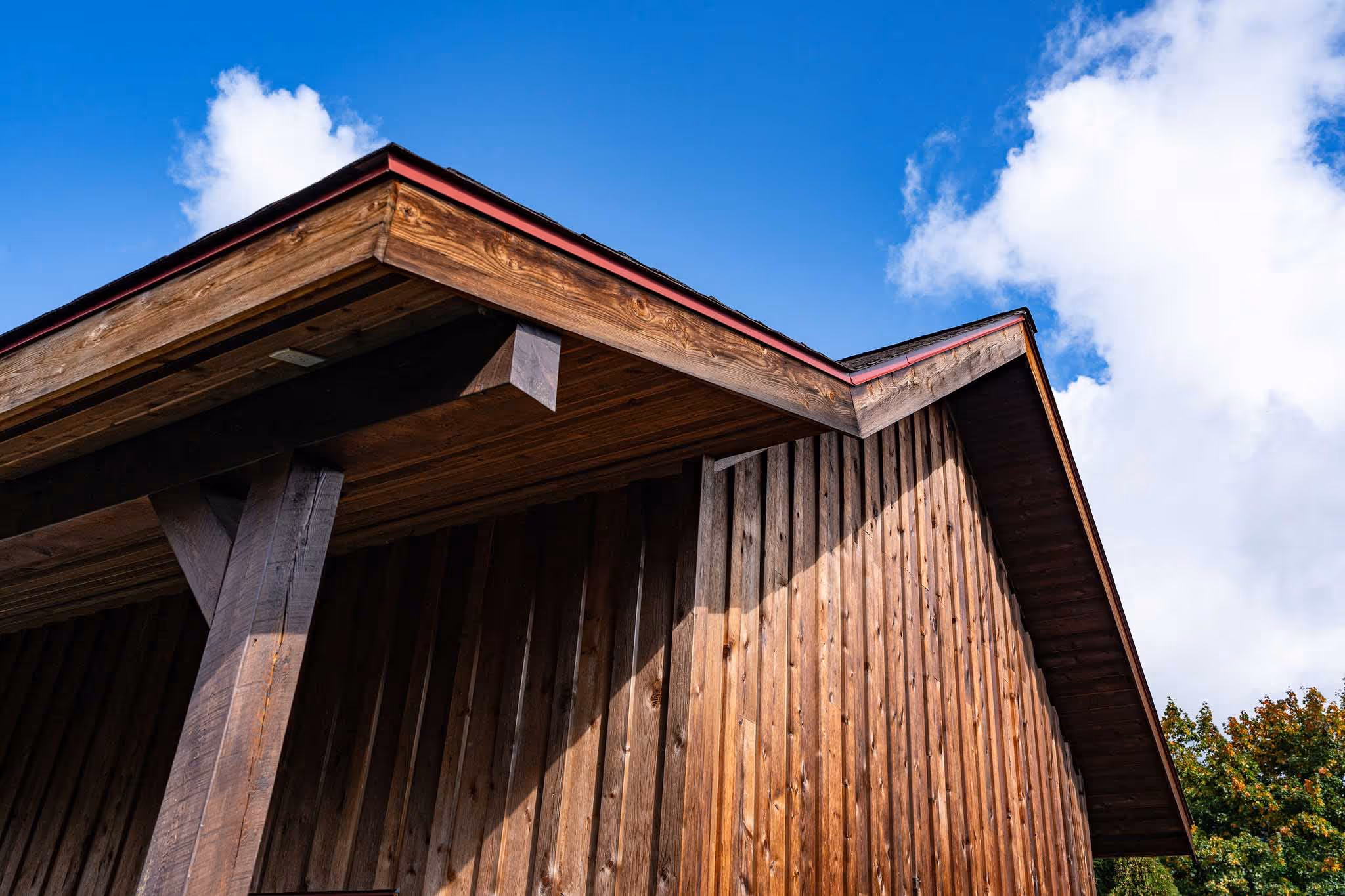 Roof and overhand of wooden garage, blue sky in background.