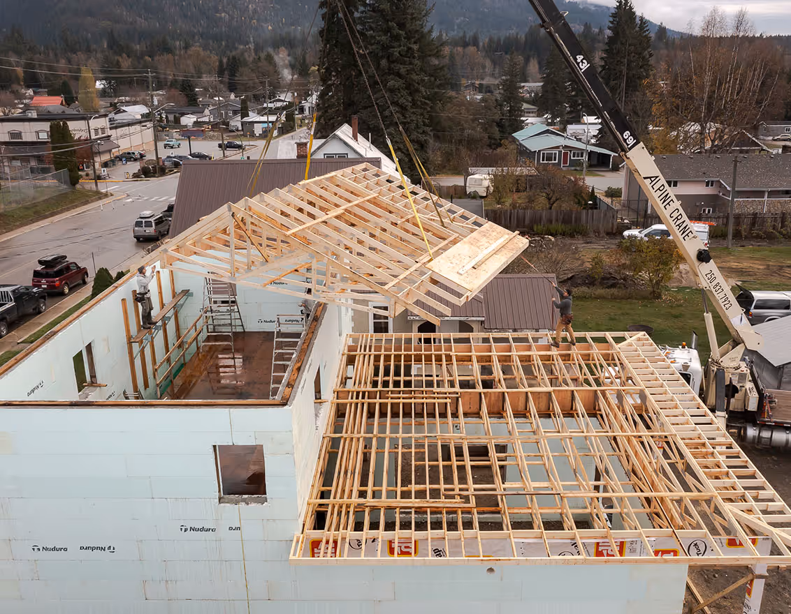 Construction workers using a crane to lift a wooden roof frame onto a house under construction in a residential area.