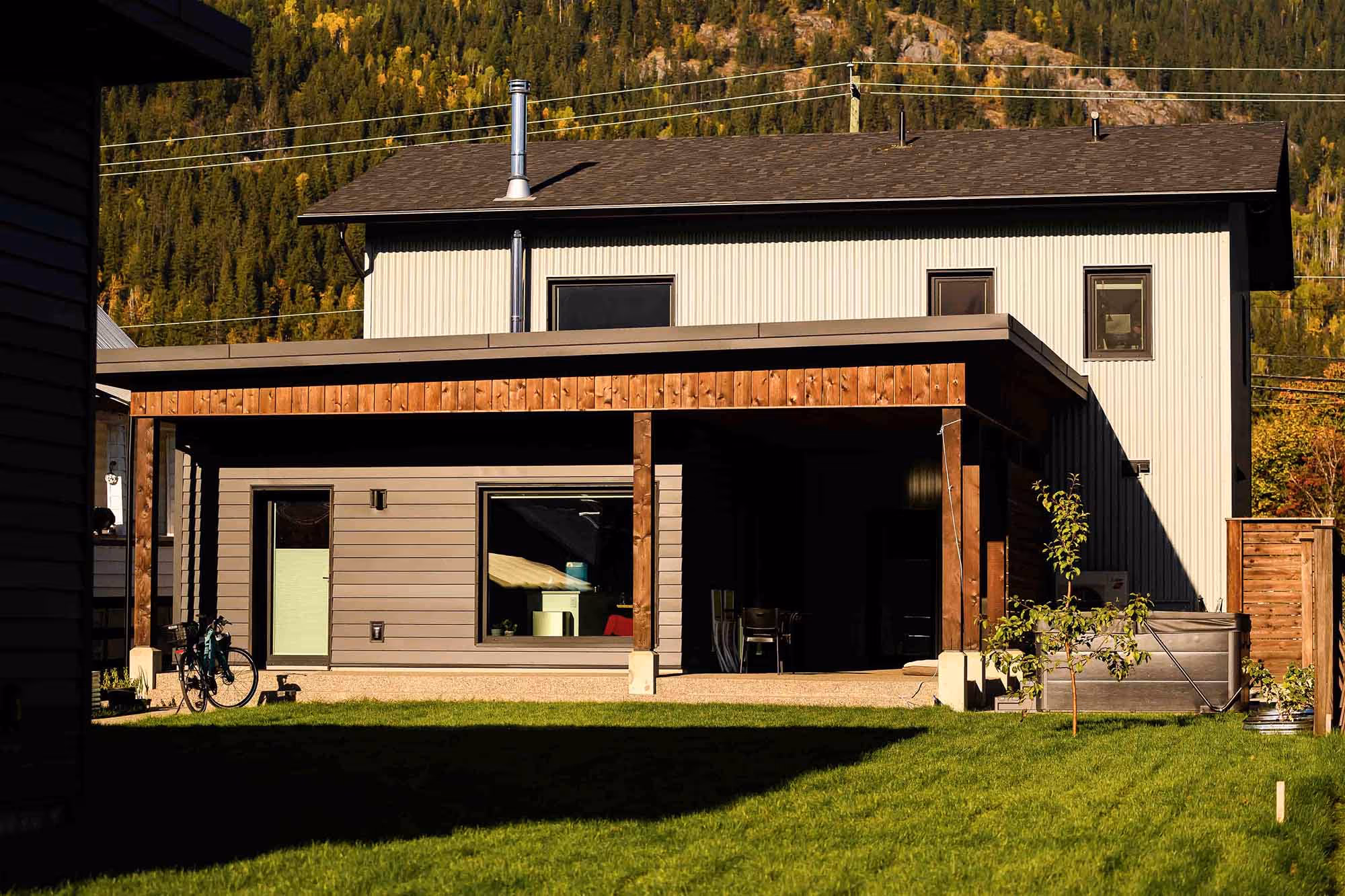 Modern two-story house with wood and beige siding, a covered porch, green lawn, and a bicycle parked near the side.