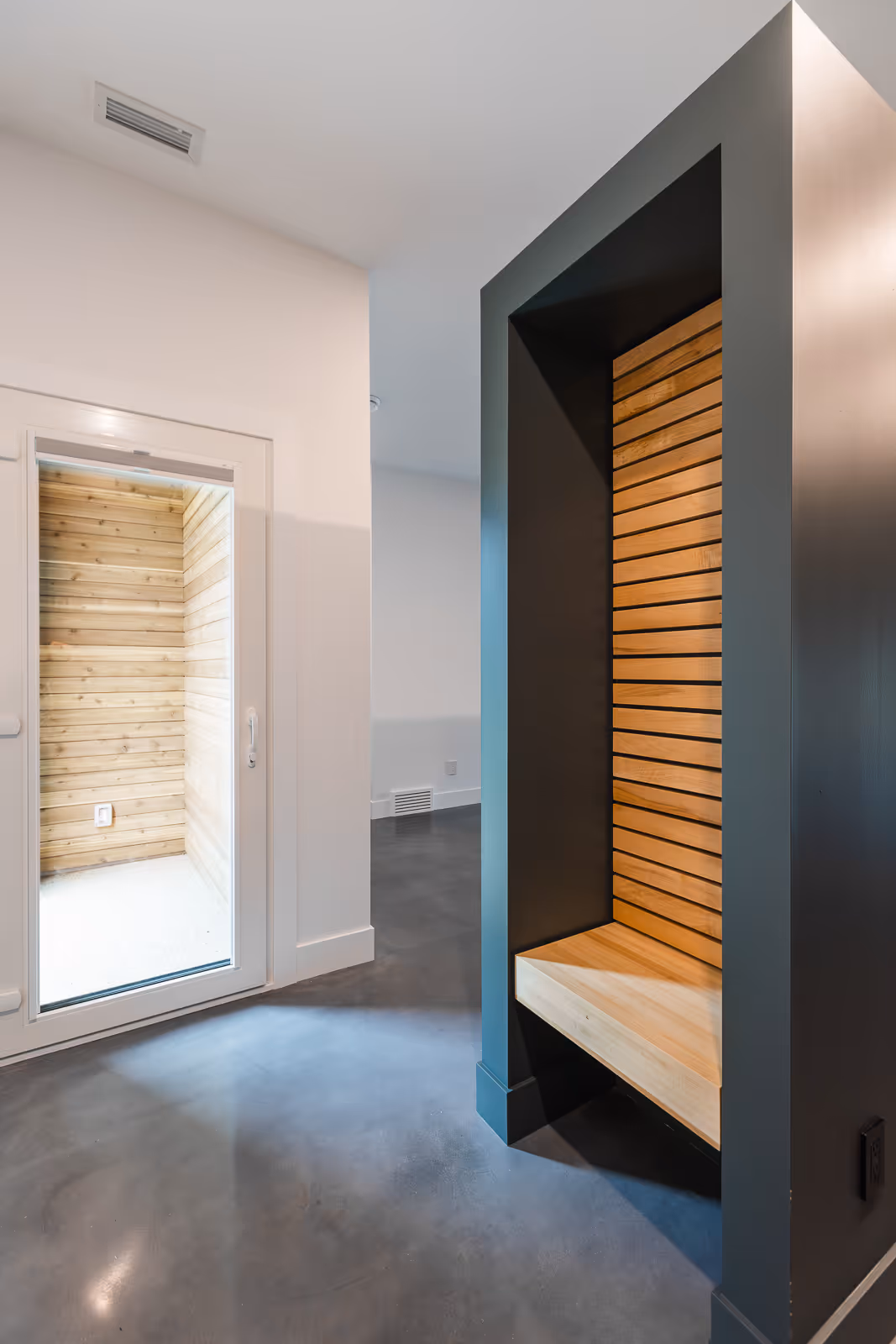 Modern entryway featuring a built-in wooden slat bench with dark framing and glass door leading to a wood-paneled space.
