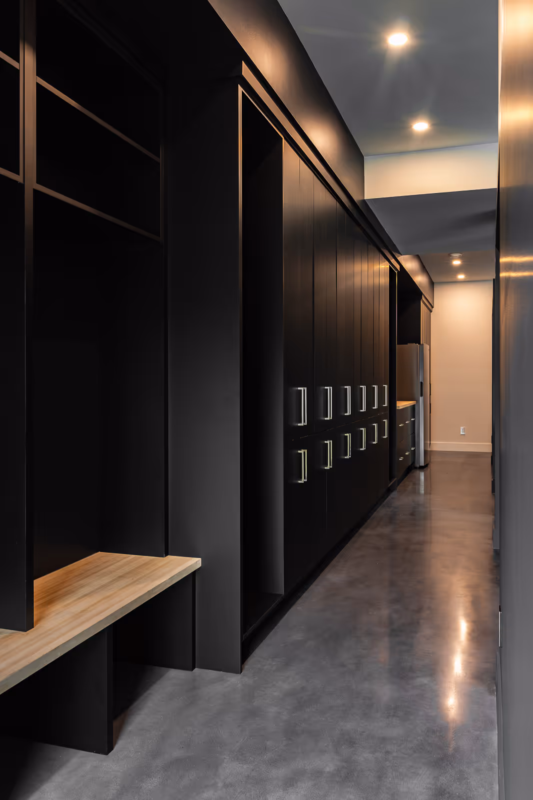 Modern hallway with black cabinets, wooden bench, concrete floor, and recessed ceiling lights.