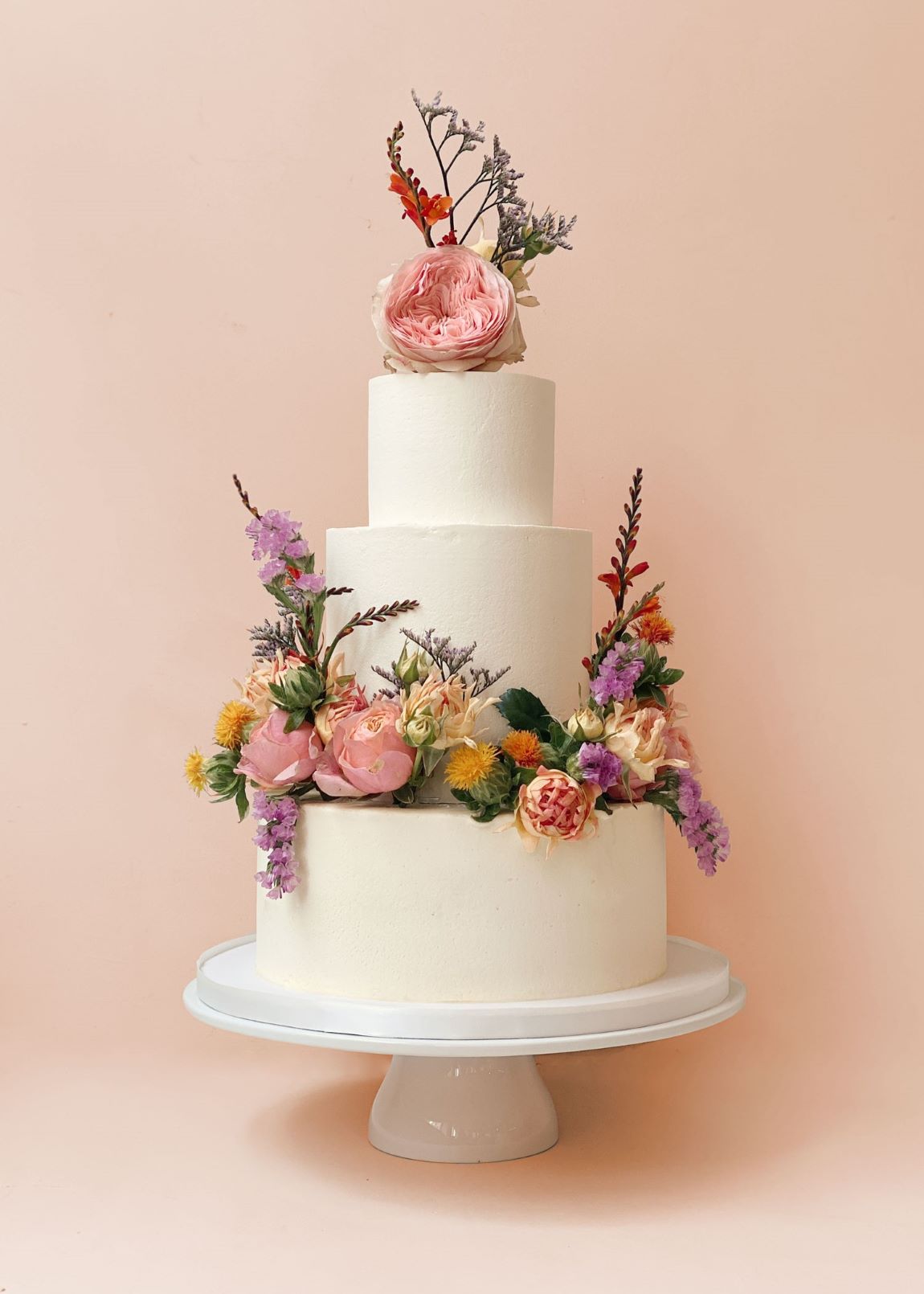 3-tier white buttercream coated wedding cake decorated with vibrant fresh bloom