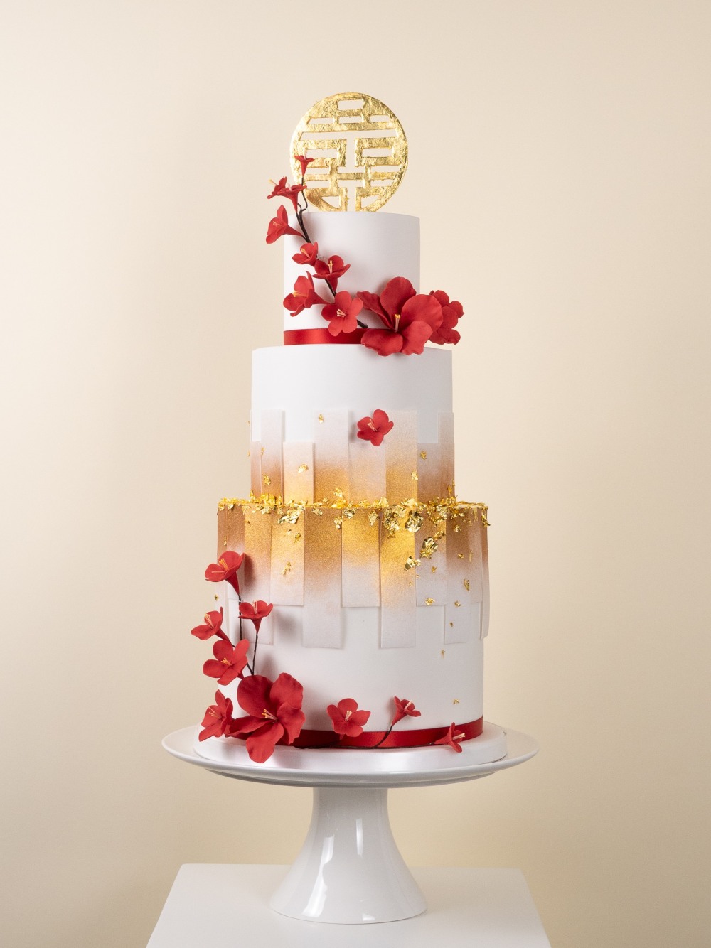 Three tier Chinese inspired wedding cake with handcrafted red cherry blossoms and a golden double happiness symbol topper.
