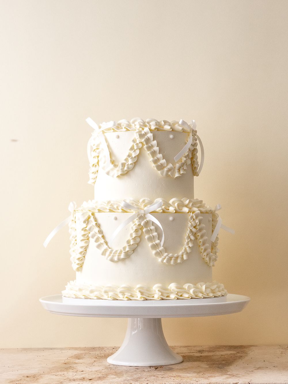 Two tier ivory wedding cake with Lambeth style piped ruffle swags, scalloped borders, and satin bows.