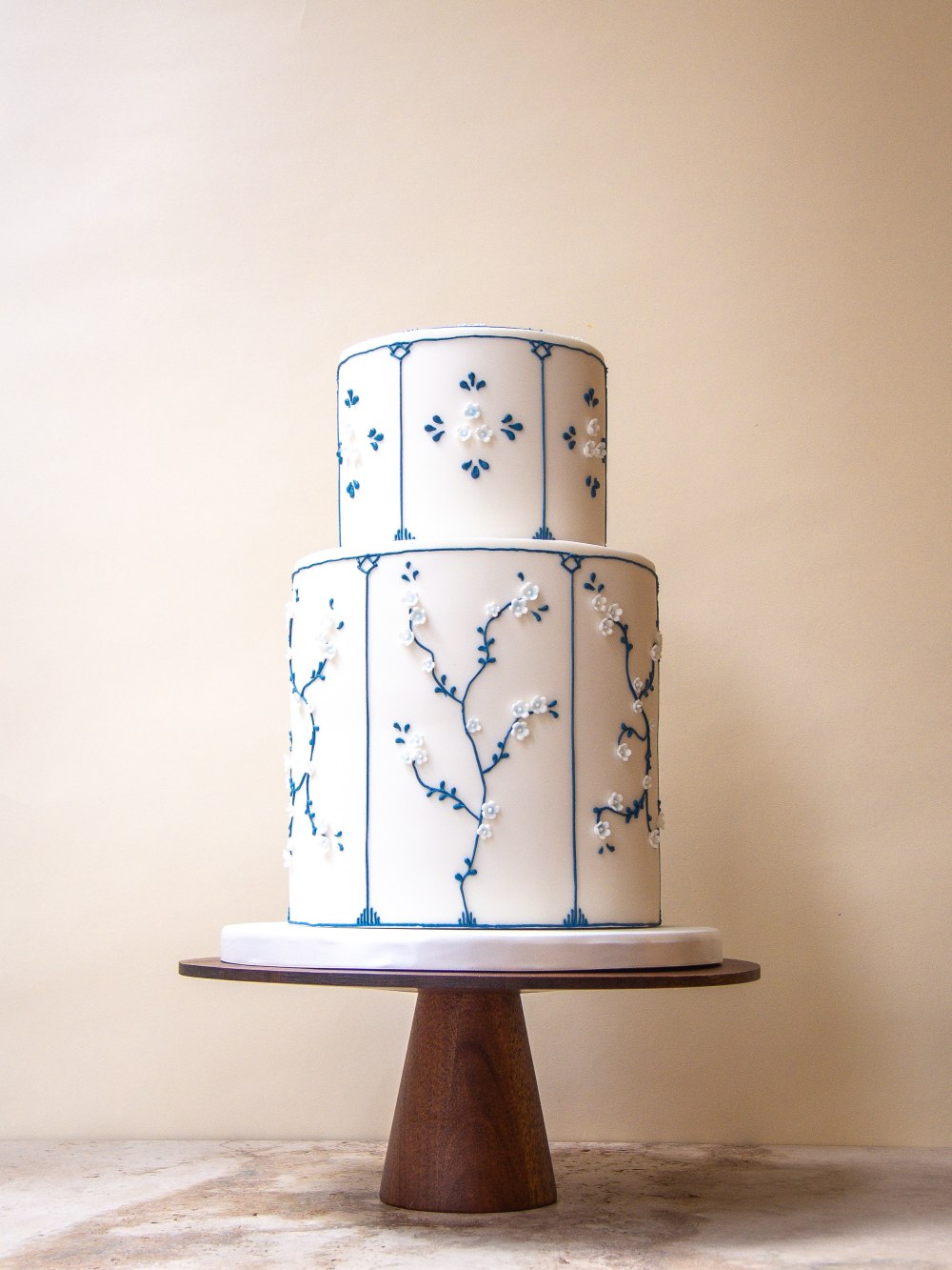 Two tier white wedding cake hand piped in Delft blue with panelled detailing, delicate motifs, and handcrafted white sugar blossoms.