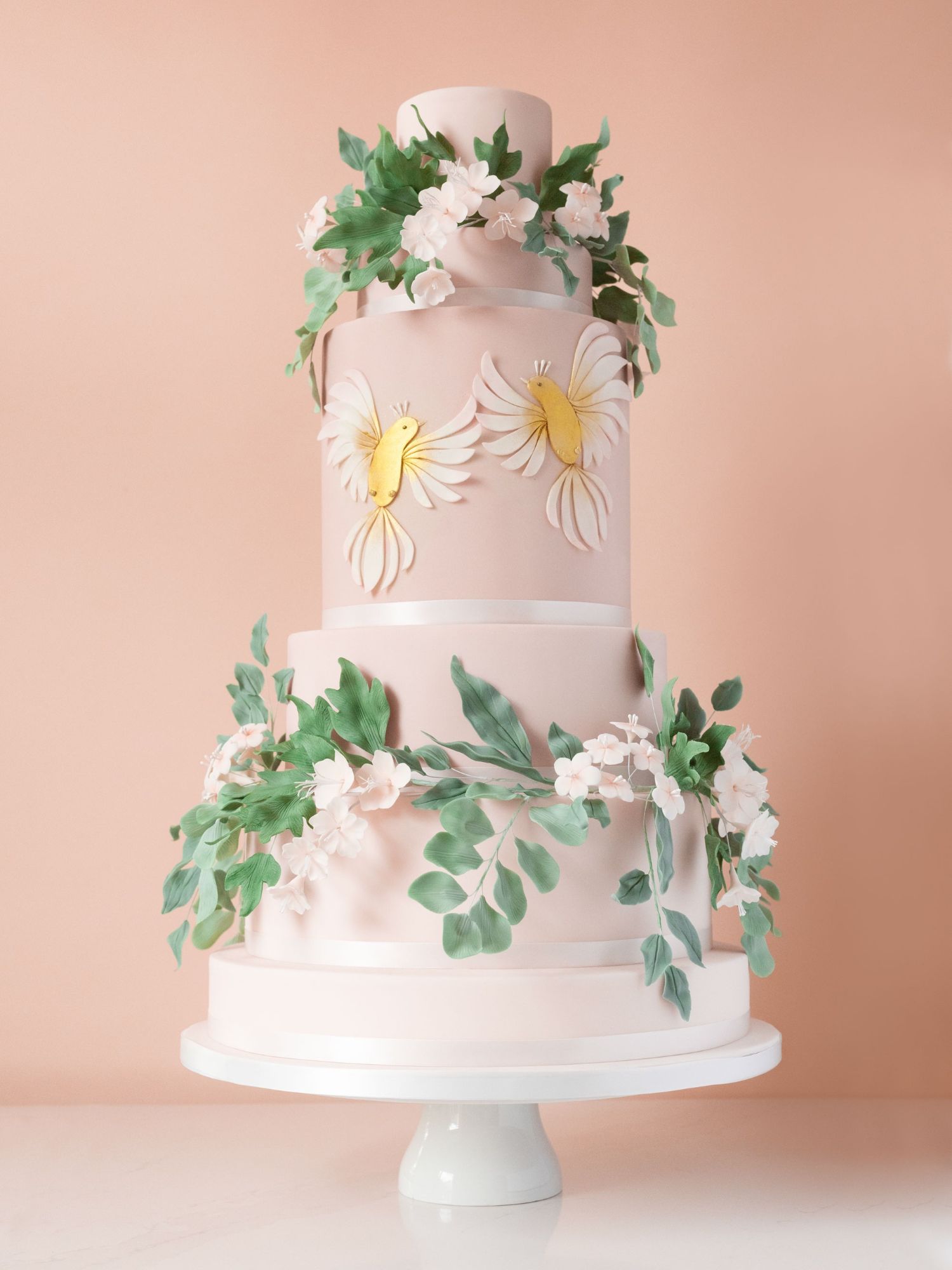 Beautiful wedding cake decorated with trailing sugar flowers and leaves, adorned with two golden love birds as centre point. 