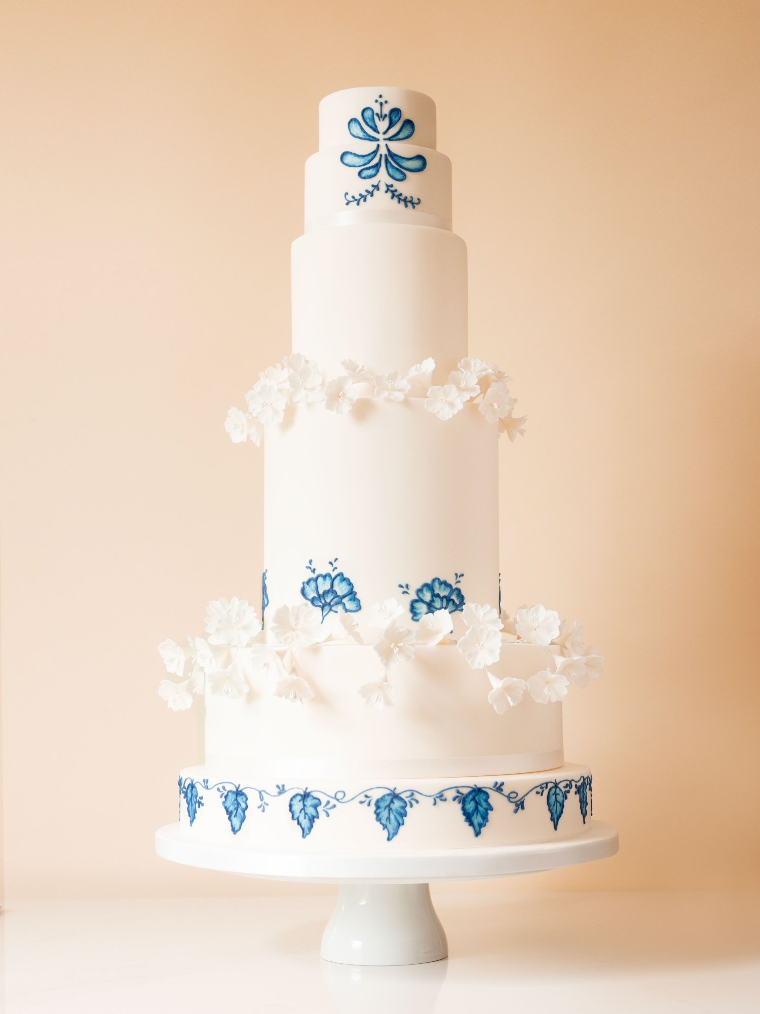 Beautiful 6-tier white wedding cake with blue delft embroidery piping and wreaths of delicate white sugar blossoms. 