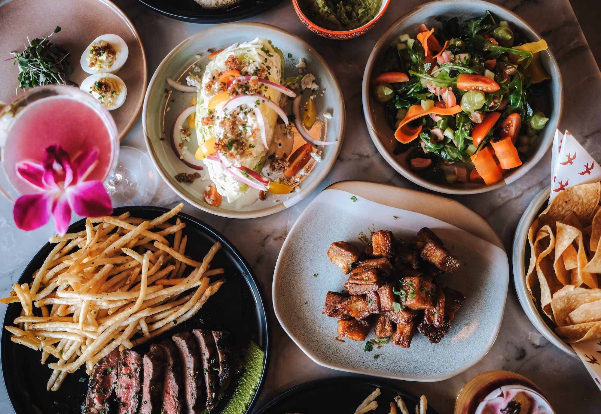 A table spread of shared plates, salads, fries and steak