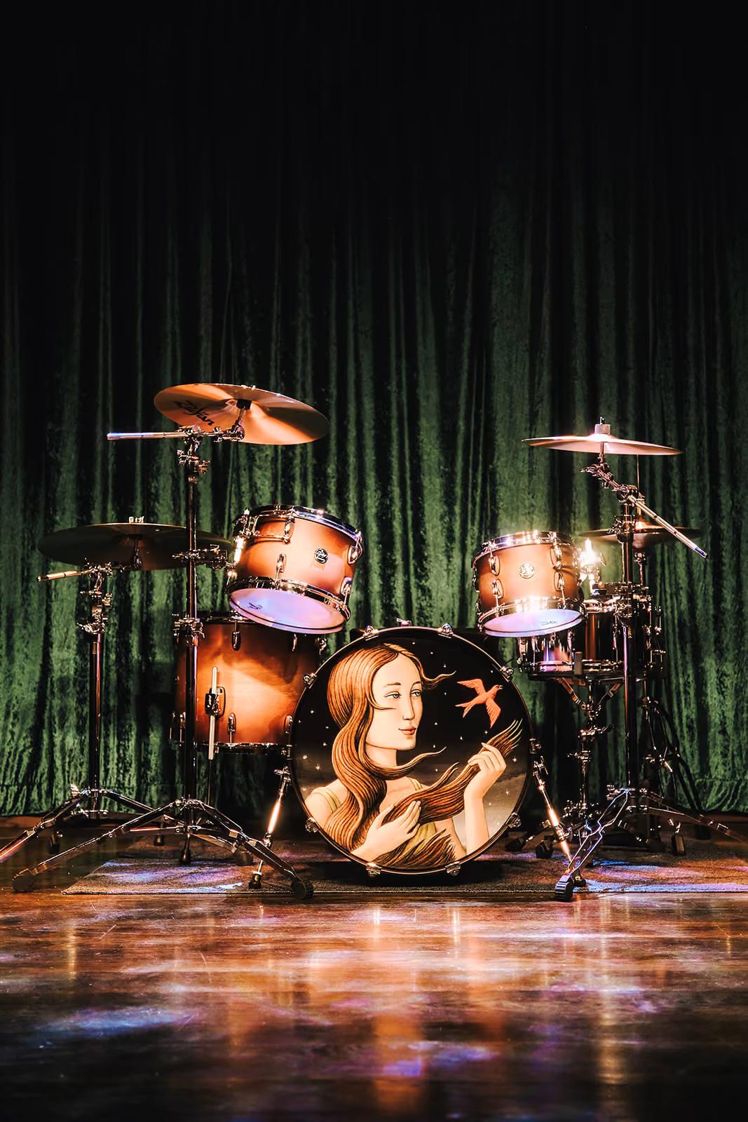 A drum kit on the Music Room stage in front of green velvet curtains