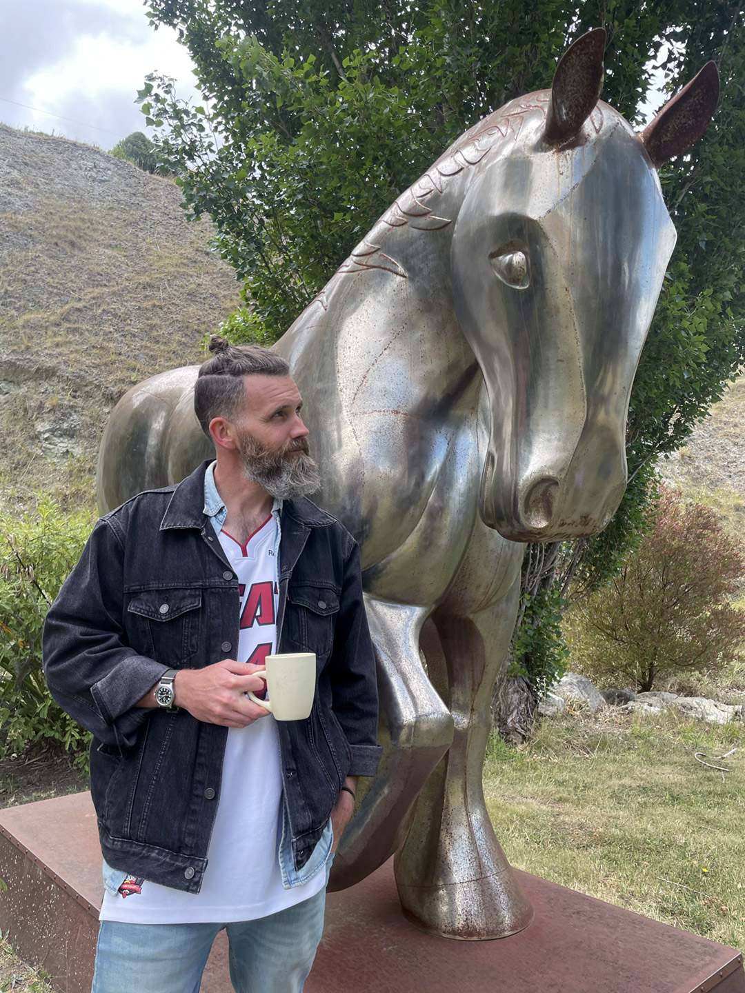 HOOF founder Erik Hay standing with a cup of tea in front of a giant silver horse sculpture.