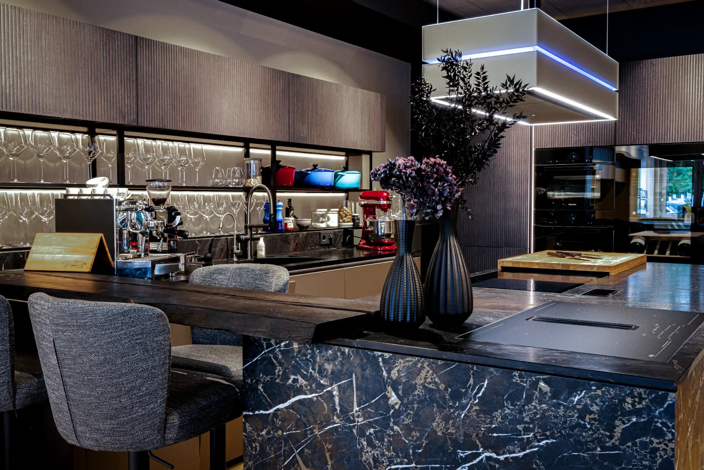 Moderne Kücheninsel verbunden durch eine Theke aus echter Mooreiche mit Baumkante. Setzen Sie sich an unsere Kaffeebar und fühlen Sie sich unter Freunden im Thoki Küchenstudio