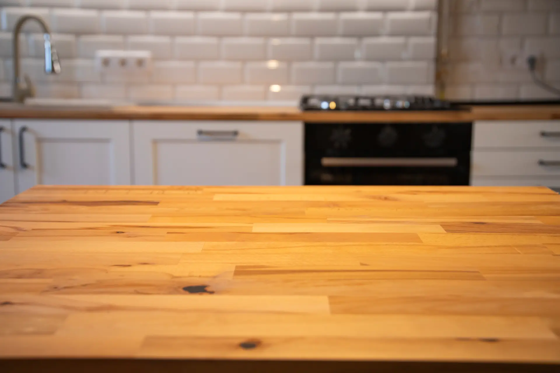 Nahaufnahme einer sauberen Küchenarbeitsplatte aus Holz, im Hintergrund weiße Küchenmöbel und Fliesen – Tipps, wie du deine Küchenarbeitsplatte richtig reinigen kannst.